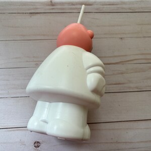 Peut inclure: Une figurine en plastique blanche repr&eacute;sentant une personne avec une t&ecirc;te rose et une paille qui sort du haut. La figurine porte un manteau blanc et a un bras blanc avec un gant blanc.