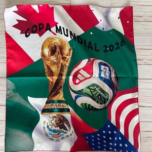 May include: A square fabric with a soccer theme. It features the FIFA World Cup trophy, a soccer ball, and flags of the United States, Canada, and Mexico. The text "COPA MUNDIAL 2026" is also present.