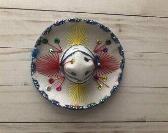 May include: A white sombrero with blue, red, yellow, and green embroidery and sequins.