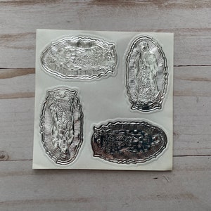 May include: Four silver foil stickers featuring an image of the Virgin Mary. The stickers are on a white sheet of paper.