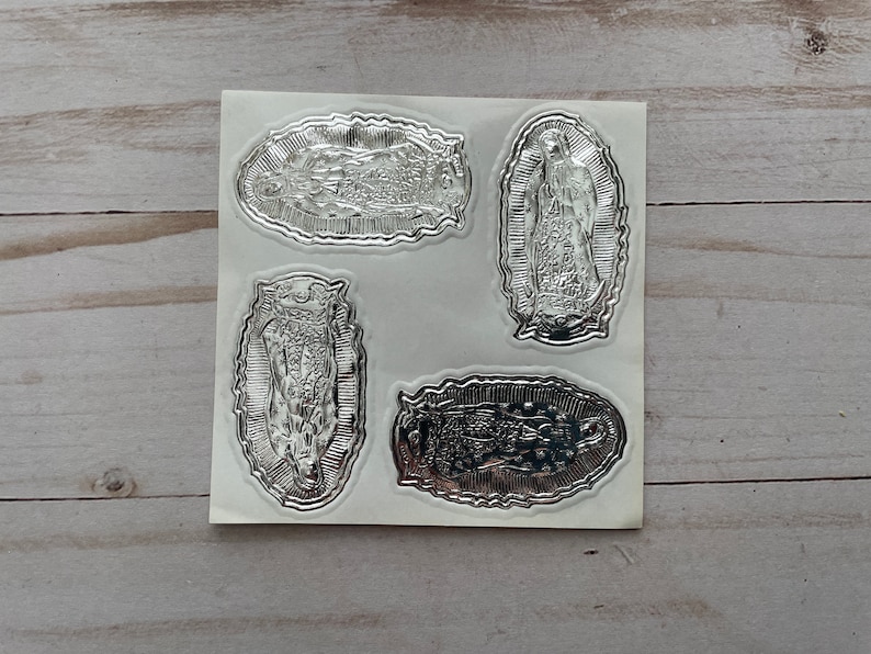 May include: Four silver foil stickers featuring an image of the Virgin Mary. The stickers are on a white sheet of paper.