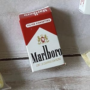 May include: A pack of Marlboro Filter Cigarettes. The pack is red and white with the Marlboro logo in black. The text "FILTER CIGARETTES" is printed on the top of the pack.