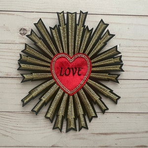 May include: A red velvet heart with the word "LOVE" embroidered on it, surrounded by a gold and black embroidered sunburst design.