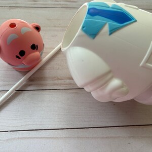 Peut inclure: Une figurine en c&eacute;ramique rose et blanche avec un trou en haut, une paille blanche et une figurine en c&eacute;ramique blanche avec un motif de cravate bleue.