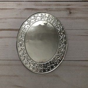 May include: Silver oval-shaped charger plate with a decorative floral design around the edge.