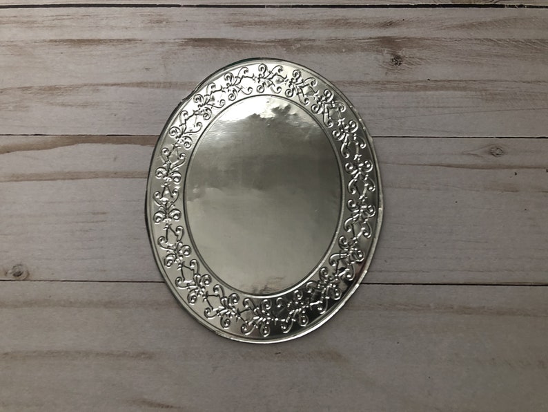 May include: Silver oval-shaped charger plate with a decorative floral design around the edge.