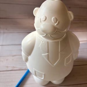 Peut inclure: Figurines en plastique blanc d'une personne avec une moustache et un costume. La figurine est debout sur une surface en bois.