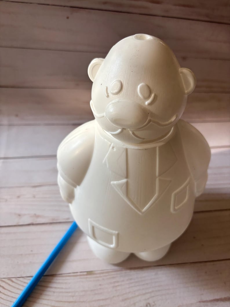 Peut inclure: Figurines en plastique blanc d'une personne avec une moustache et un costume. La figurine est debout sur une surface en bois.