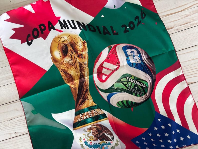 May include: A decorative scarf featuring the FIFA World Cup trophy and a soccer ball. The scarf has the text "COPA MUNDIAL 2026" and includes flags of the United States, Mexico, and Canada. The soccer ball has the word "TRIONDA" on it.