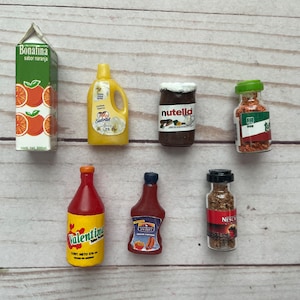 May include: A collection of miniature food items, including a bottle of orange juice labeled "Bonafina sabor naranja", a bottle of yellow dish soap labeled "Suavitel", a jar of chocolate spread labeled "Nutella", a bottle of red sauce labeled "Valentina", a bottle of brown sauce labeled "Caliente", a jar of spices labeled "Nescafé", and a jar of spices labeled "Tetilla".
