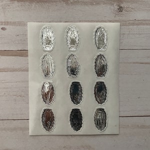 May include: A sheet of silver stickers featuring an image of the Virgin Mary. The stickers are arranged in a grid pattern on a white background.