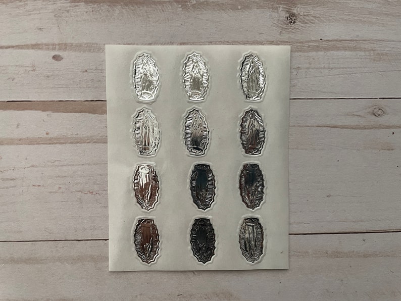 May include: A sheet of silver stickers featuring an image of the Virgin Mary. The stickers are arranged in a grid pattern on a white background.