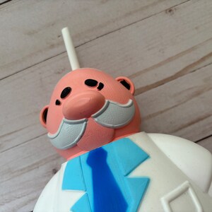 Peut inclure: Un gobelet en plastique rose et blanc en forme de personnage de dessin anim&eacute; avec une paille blanche. Le personnage a une moustache blanche, une cravate bleue et une blouse de laboratoire blanche.