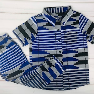 May include: A matching set of children's clothing, including a short-sleeved button-down shirt and pants. The fabric features a blue, black, and white geometric pattern. The shirt has a collar and buttons down the front. The pants have an elastic waistband.