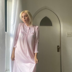 May include: A woman wearing a pink, long-sleeved nightgown with white lace trim and a button-up front.