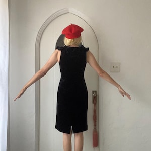 Puede incluir: Una mujer con un vestido de terciopelo negro y una boina roja. El vestido tiene un escote con volantes y una silueta ajustada.