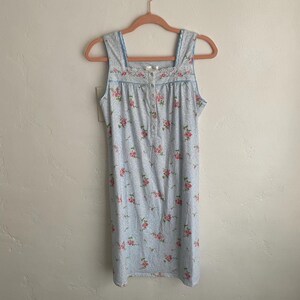 May include: A light blue nightgown with a floral pattern of pink roses. The sleeveless dress has a square neckline with lace trim and a button-down front. The nightgown is hanging on a pink hanger.
