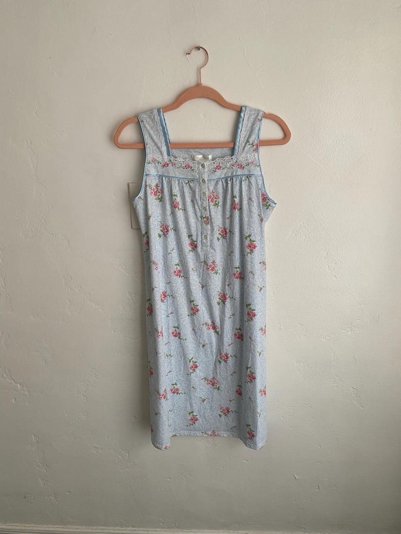 May include: A light blue nightgown with a floral pattern of pink roses. The sleeveless dress has a square neckline with lace trim and a button-down front. The nightgown is hanging on a pink hanger.