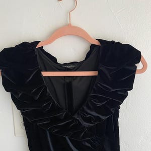 Puede incluir: Vestido negro de terciopelo con escote de volantes y silueta ajustada.