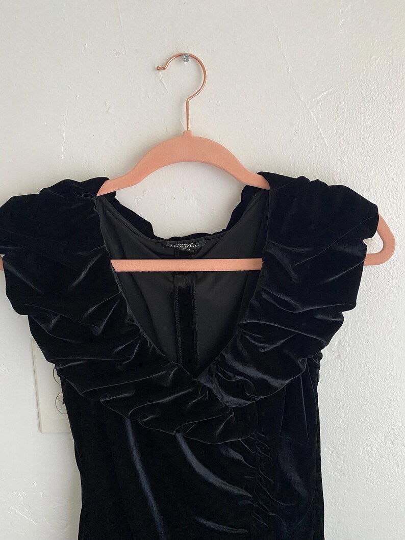 Puede incluir: Vestido negro de terciopelo con escote de volantes y silueta ajustada.