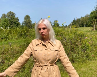 May include: A beige trench coat with a belt and a pattern of small white and yellow circles. The coat has a collar and long sleeves.