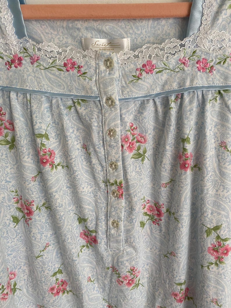 May include: Light blue paisley print nightgown with pink floral embroidery and lace trim. The nightgown has a button-down front and a scoop neckline. The label reads "Secret Treasures Sleepwear".