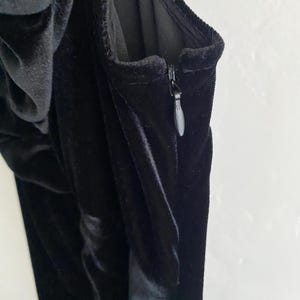 Puede incluir: Un vestido de terciopelo negro con cierre de cremallera. El vestido tiene un corpi&ntilde;o ajustado y una falda fluida.