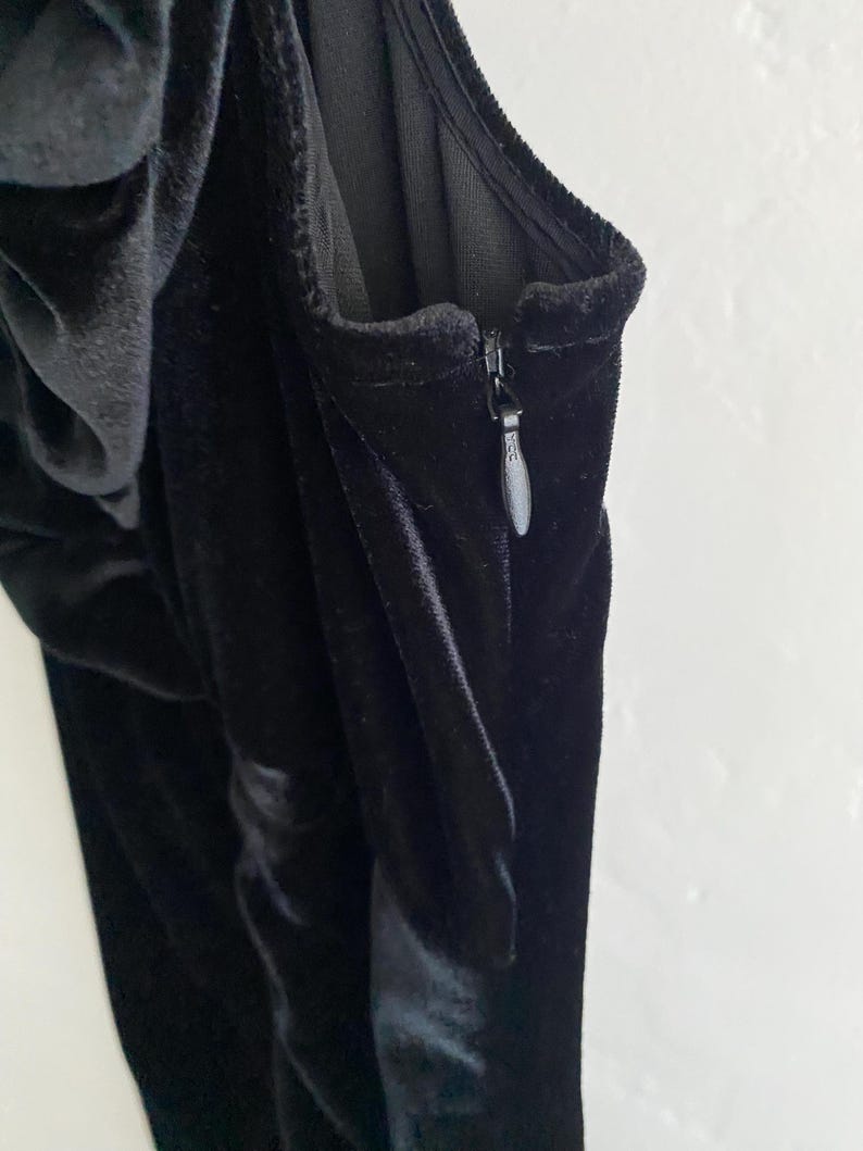 Puede incluir: Un vestido de terciopelo negro con cierre de cremallera. El vestido tiene un corpi&ntilde;o ajustado y una falda fluida.