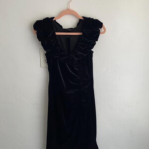 Puede incluir: Un vestido de terciopelo negro con un escote de volantes y sin mangas.