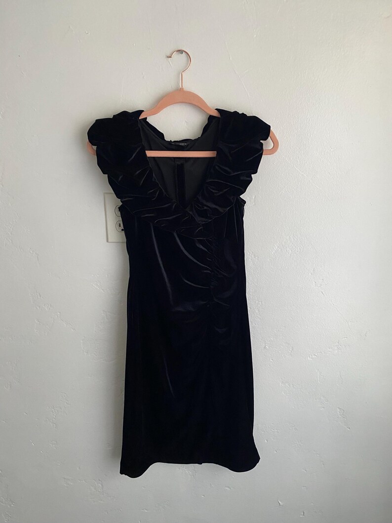 Puede incluir: Un vestido de terciopelo negro con un escote de volantes y sin mangas.