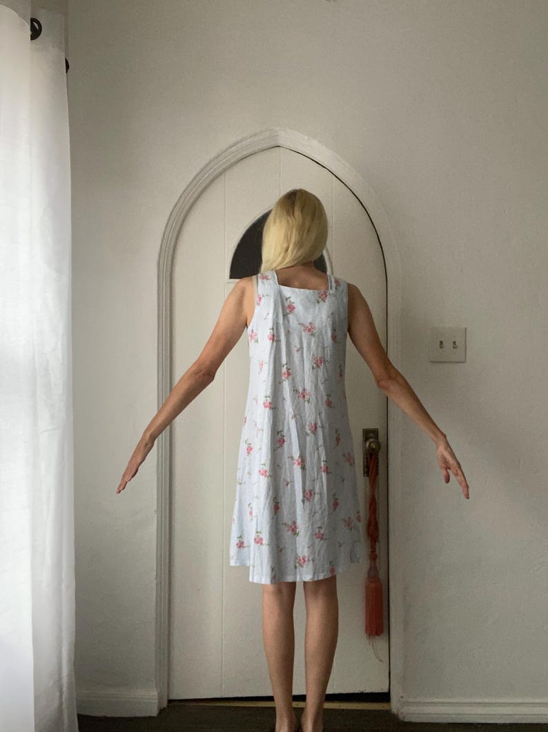 May include: A light blue sundress with a floral pattern of pink roses. The dress has a square neckline and a simple, A-line silhouette. The fabric appears to be lightweight, suitable for warm weather.