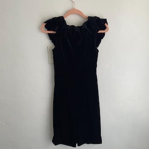 Puede incluir: Un vestido de terciopelo negro con un escote de volantes y mangas cortas.