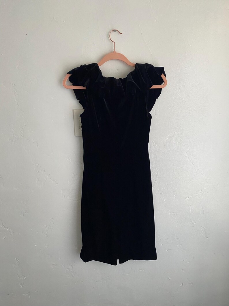 Puede incluir: Un vestido de terciopelo negro con un escote de volantes y mangas cortas.
