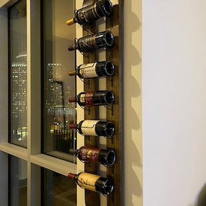 May include: A wooden wine rack with six bottles of wine. The rack is mounted on a wall and has a dark brown finish. The bottles are arranged in a vertical row.