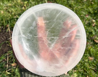May include: A white selenite crystal bowl with a smooth, polished surface. The bowl has a natural, organic shape and is perfect for holding crystals, jewelry, or other small items.