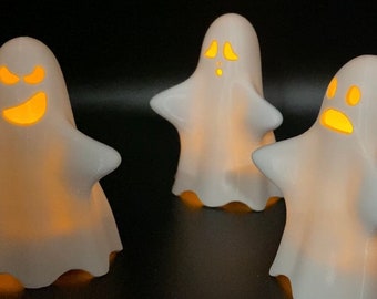 May include: Three white ceramic ghost figurines with glowing orange eyes. The ghosts are illuminated from within, creating a spooky and festive Halloween atmosphere.