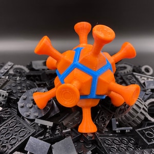 May include: A bright orange and blue 3D printed model of a virus, sitting on a pile of black Lego bricks.