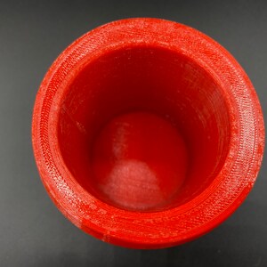 May include: A red plastic cup with a smooth, rounded interior and a textured exterior. The cup is empty and appears to be made with a 3D printer.