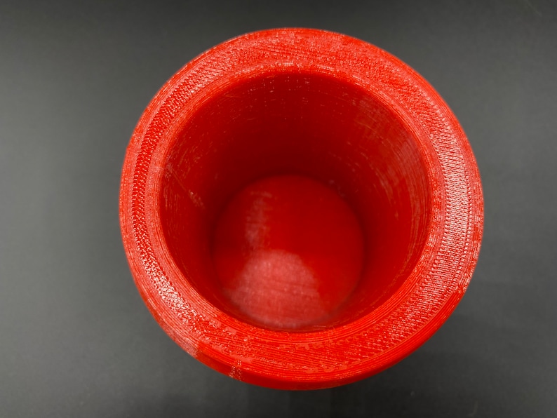 May include: A red plastic cup with a smooth, rounded interior and a textured exterior. The cup is empty and appears to be made with a 3D printer.