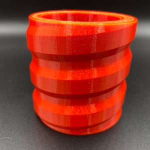 May include: A bright orange, 3D printed, cylindrical container with a textured, ridged design.