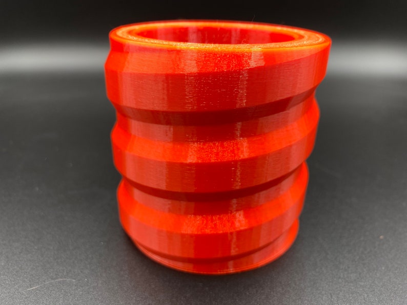 May include: A bright orange, 3D printed, cylindrical container with a textured, ridged design.