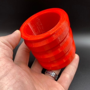 May include: A bright orange 3D printed cylindrical object with a textured surface. The object is hollow and has a slightly flared opening at the top.