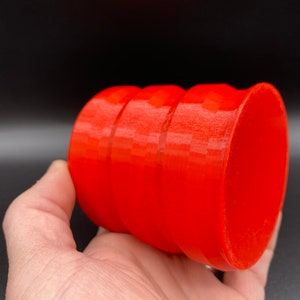 May include: A bright red, cylindrical container with a smooth, glossy finish. The container has three distinct bands around its circumference.