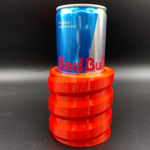 May include: A red 3D printed can holder with a blue and silver Red Bull can inside.