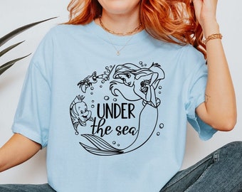May include: A light blue t-shirt with a black graphic of Ariel from The Little Mermaid, Flounder, and Sebastian. The graphic includes the text "Under the Sea".