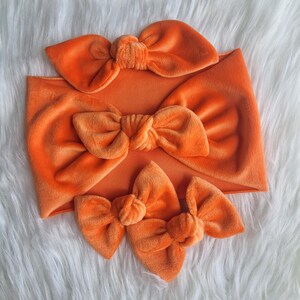 Peut inclure: Trois nœuds en velours orange de différentes tailles. Le plus grand nœud est attaché à un bandeau.