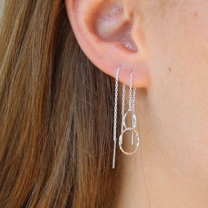 May include: A silver chain earring with three dangling chains, including a small circle and a longer, straight chain.