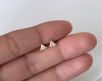 May include: A pair of gold triangle stud earrings with clear cubic zirconia stones.