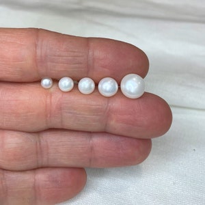 May include: A set of seven white pearls of varying sizes, arranged in order from smallest to largest, on a hand.