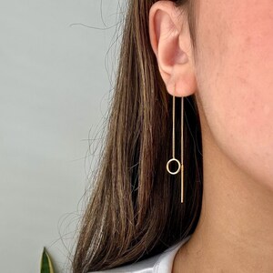 May include: Gold chain earrings with a small circle and a straight line pendant.